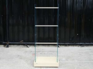 Product hanging rack Product hanging shelf, glass walls on 2 sides, 3 hanging rails, cream colored wooden base.