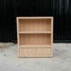 Product shelf, 2-level shelves, 2 storage cabinets with open doors, light brown wooden frame.