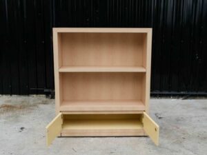 Product shelf, 2-level shelves, 2 storage cabinets with open doors, light brown wooden frame.