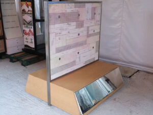 Product shelves, display stands, 2 sides, brown wooden base. Has a drawer in front of a mirror and has wheels