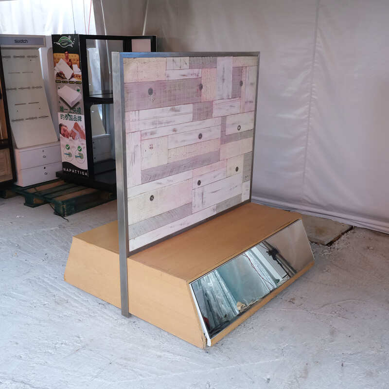 Product shelves, display stands, 2 sides, brown wooden base. Has a drawer in front of a mirror and has wheels