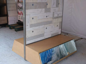 Product shelves, display stands, 2 sides, brown wooden base. Has a drawer in front of a mirror and has wheels