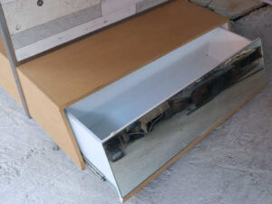 Product shelves, display stands, 2 sides, brown wooden base. Has a drawer in front of a mirror and has wheels