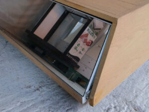 Product shelves, display stands, 2 sides, brown wooden base. Has a drawer in front of a mirror and has wheels