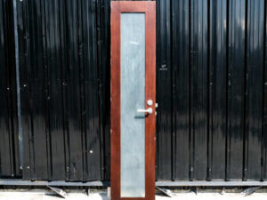 Tall, narrow wooden door, glass panel, lever-type knob.