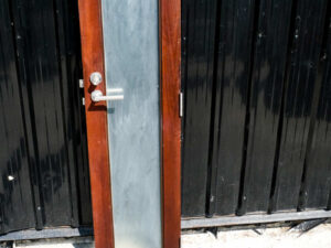 Tall, narrow wooden door, glass panel, lever-type knob.