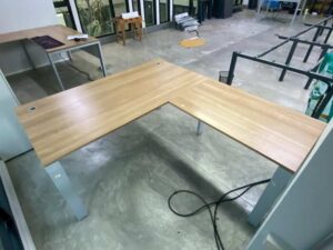 L-shaped corner desk with steel legs and light brown wood top, includes power strip. PROFLEX brand.