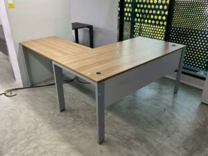L-shaped corner desk with steel legs and light brown wood top, includes power strip. PROFLEX brand.