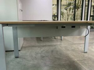 L-shaped corner desk with steel legs and light brown wood top, includes power strip. PROFLEX brand.