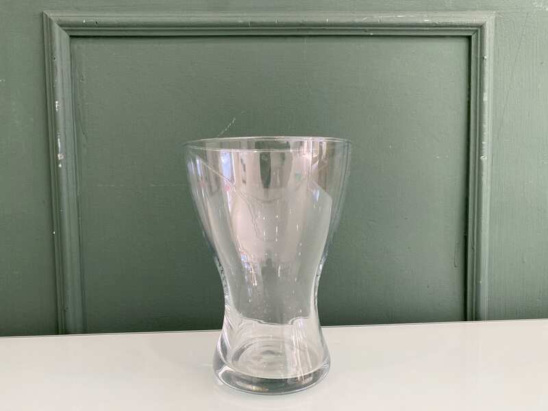 A clear glass flower vase, shaped like an hourglass.
