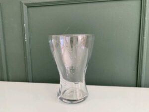 A clear glass flower vase, shaped like an hourglass.