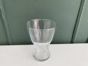 A clear glass flower vase, shaped like an hourglass.