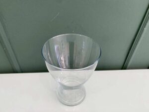 A clear glass flower vase, shaped like an hourglass.