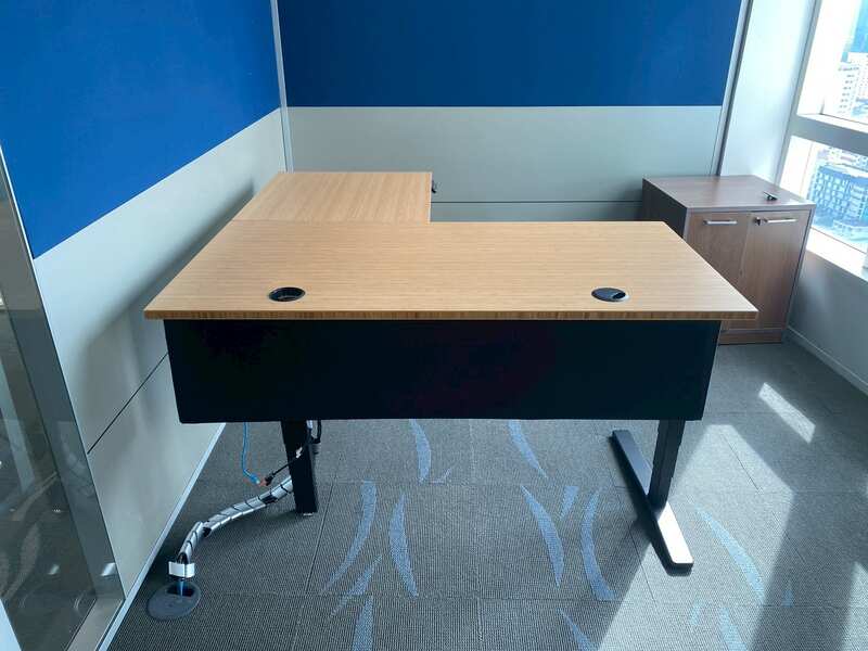 Uplift Desk, adjustable standing desk, L-shaped, black steel legs, with power strip, 150 cm wide.