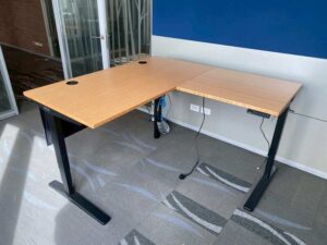 Uplift Desk, adjustable standing desk, L-shaped, black steel legs, with power strip, 150 cm wide.