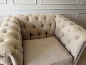Chesterfield style armchair with cream-colored fabric and button tufting. (1)