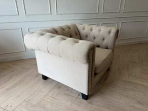 Chesterfield style armchair with cream-colored fabric and button tufting. (1)