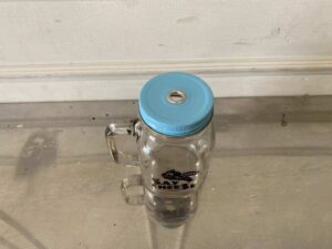Clear glass mason jar with handle and lid.