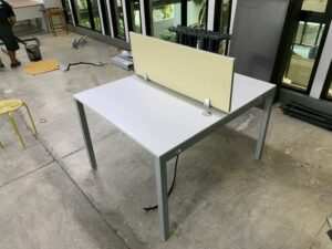 Two-seater group workstation with grey steel legs, cream-colored partition, and power strip.
