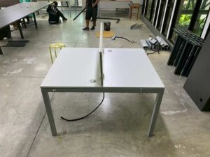 Two-seater group workstation with grey steel legs, cream-colored partition, and power strip.