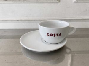 White ceramic coffee cup set with handle and saucer, Costa Coffee brand.