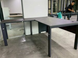 L-shaped corner desk with steel legs and dark brown wood top, with power strip.