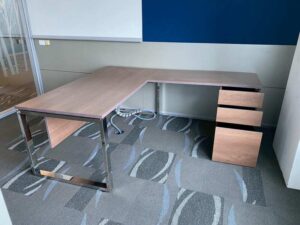 L-shaped corner desk with 3 drawers, steel legs, with rails, and power outlet.