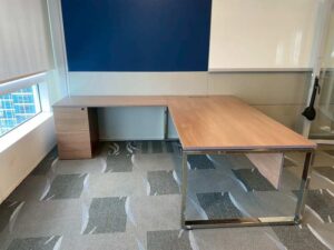 L-shaped corner desk with 3 drawers, steel legs, with rails, and power outlet.